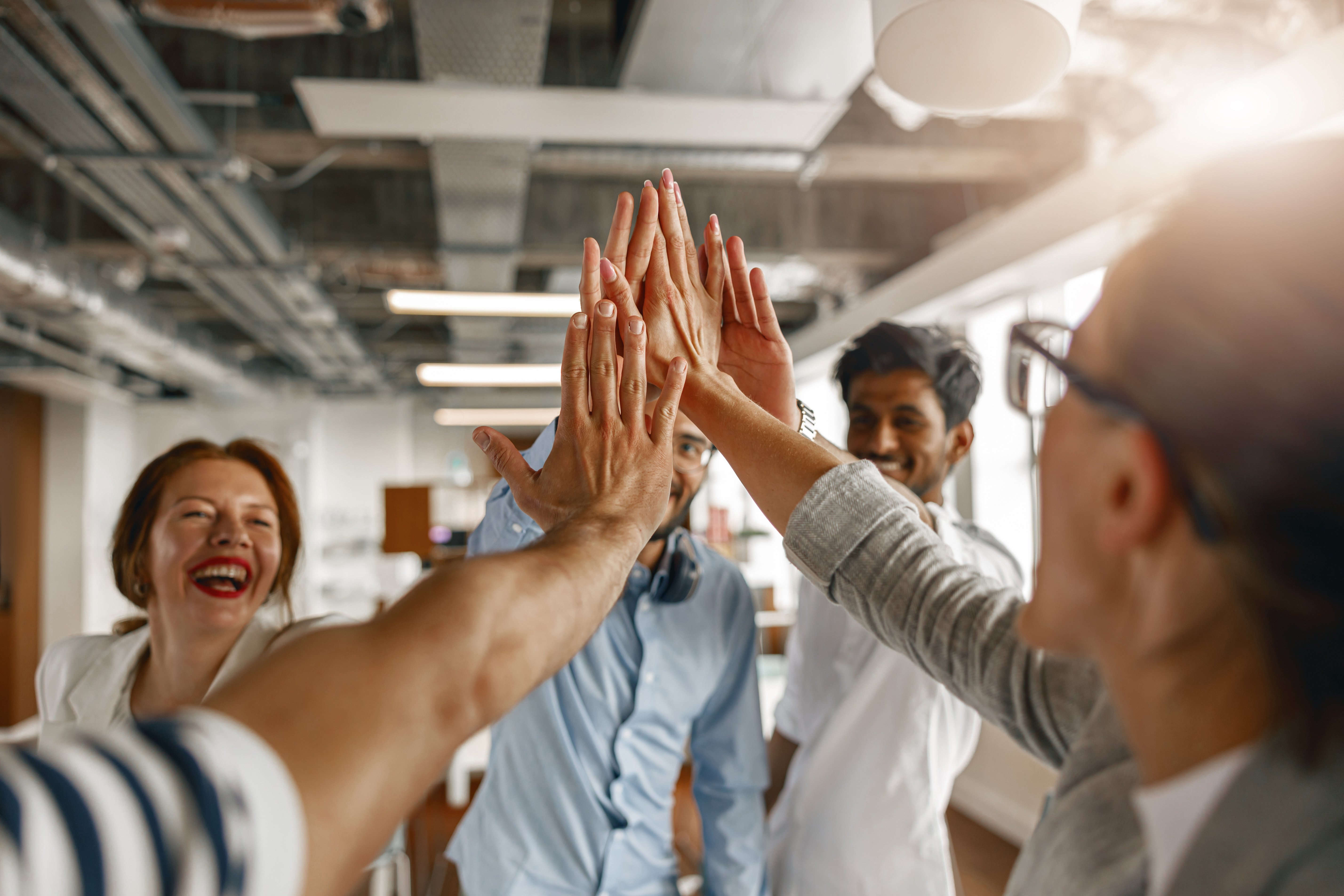 Team members joining hands in a high-five during a collaborative workplace meeting, symbolizing trust, teamwork and high performance.